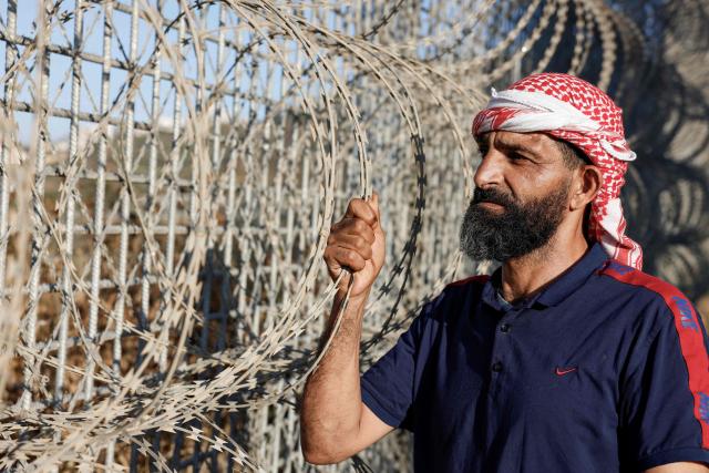 Palestinian anti-Israeli settlement activist Ayed Ghafri, from the town of Sinjil, north of Ramallah in the Israeli-occupied Palestinian West Bank, poses for a photograph near a huge fence erected by Israelis surrounding the town, which residents say has imposed further restrictions on their movement and access to their agricultural lands on June 15, 2026. Repeated attacks by Israeli settlers have made access to and cultivation of the land increasingly perilous. The occupied West Bank has been gripped by almost daily violence involving Israeli troops and settlers since the start of the Gaza war in October 2023. (Photo by Zain JAAFAR / AFP)