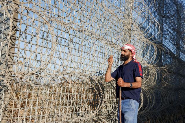 Palestinian anti-Israeli settlement activist Ayed Ghafri, from the town of Sinjil, north of Ramallah in the Israeli-occupied Palestinian West Bank, poses for a photograph near a huge fence erected by Israelis surrounding the town, which residents say has imposed further restrictions on their movement and access to their agricultural lands on June 15, 2026. Repeated attacks by Israeli settlers have made access to and cultivation of the land increasingly perilous. The occupied West Bank has been gripped by almost daily violence involving Israeli troops and settlers since the start of the Gaza war in October 2023. (Photo by Zain JAAFAR / AFP)