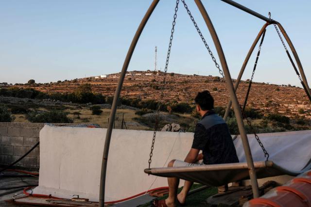 A Palestinian man sits on a swing on the rooftop of his home overlooking a newly established Israeli settlement outpost north of the town of Sinjil, north of Ramallah in the occupied West Bank, on June 15, 2026. The occupied West Bank has been gripped by almost daily violence involving Israeli troops and settlers since the start of the Gaza war in October 2023. (Photo by Zain JAAFAR / AFP)