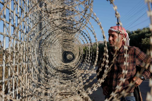 Palestinian farmer 40-year-old Mohammad Fuqaha stands near the Israeli erected fence surrounding the town of Sinjil, north of Ramallah in the Israeli occupied Palestinian West Bank, as he continues to go to his land despite restrictions on access to it on June 15, 2026. Repeated attacks by Israeli settlers have made access to and cultivation of the land increasingly perilous. The occupied West Bank has been gripped by almost daily violence involving Israeli troops and settlers since the start of the Gaza war in October 2023. (Photo by Zain JAAFAR / AFP)