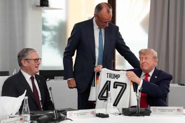 US President Donald Trump (R) reacts as he holds up a jersey of Germany's national football team bearing the number 47 and his name, gifted by Germany's Chancellor Friedrich Merz (C) flanked by Britain's Prime Minister Keir Starmer ahead of a working session at the G7 summit in Evian-les-Bains, central-eastern France on June 16, 2026. (Photo by Thibault Camus / POOL / AFP)