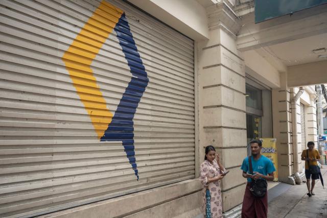 People walk past the logo of telecommunications operator MPT in Yangon on June 16, 2026. (Photo by Sai Aung MAIN / AFP)