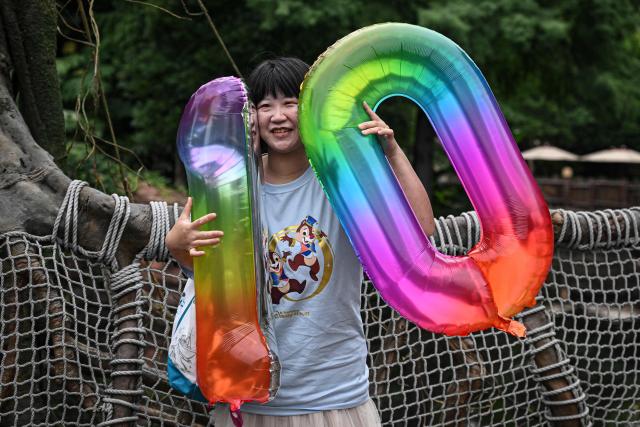 A visitor holding balloons with the number '10' is seen at Shanghai Disney Resort on its 10th anniversary in Shanghai on June 16, 2026. (Photo by Jade Gao / AFP)