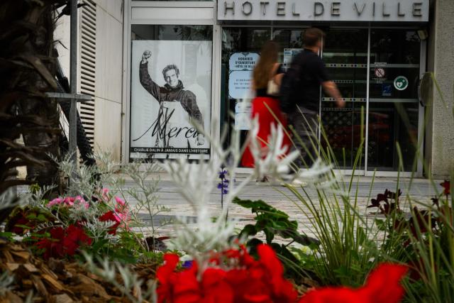 A woman and a man walk by a poster in memory of late French skipper Charlie Dalin displayed in front of the city hall, in Les Sables-d'Olonne, western France on June 16, 2026. French offshore sailor and Vendee Globe 2024/2025 winner Charlie Dalin has died in Quimper, western France, aged 42, from cancer, his family announced on June 11, 2026. (Photo by Loic VENANCE / AFP)
