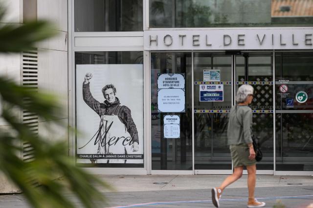 A pedestrian walks by a poster in memory of late French skipper Charlie Dalin displayed in front of the city hall, in Les Sables-d'Olonne, western France on June 16, 2026. French offshore sailor and Vendee Globe 2024/2025 winner Charlie Dalin has died in Quimper, western France, aged 42, from cancer, his family announced on June 11, 2026. (Photo by Loic VENANCE / AFP)