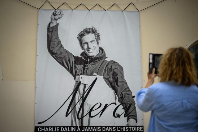 A woman takes a picture with a smartphone of a poster in memory of late French skipper Charlie Dalin displayed on the facade of the city hall in Les Sables-d'Olonne, western France on June 16, 2026. French offshore sailor and Vendee Globe 2024/2025 winner Charlie Dalin has died in Quimper, western France, aged 42, from cancer, his family announced on June 11, 2026. (Photo by Loic VENANCE / AFP)