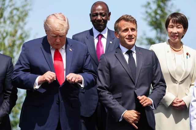US President Donald Trump and France's President Emmanuel Macron adjust their outfit during a family photograph as part of the G7 summit, in Evian, eastern France, on June 16, 2026. A G7 summit is set to take place June 15 to 17 in the French town of Evian-les-Bains near Switzerland and it will be attended by country leaders as well as the EU's foreign policy chief and ministers from Brazil, Canada, the United Arab Emirates and Turkey. (Photo by Ludovic MARIN / POOL / AFP)