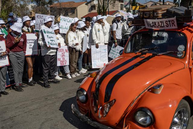 TOPSHOT - Pupils gather as a vintage Volkswagen Beetle drives past ahead of a march marking the 50th anniversary of the June 16, 1976 Soweto Uprising, organised by 1976 @ Fifty, in Soweto near Johannesburg, on June 16, 2026. June 16 is commemorated as Youth Day in South Africa, honouring the thousands of Black school students who took to the streets in 1976 to protest against the apartheid governments imposition of Afrikaans as a language of instruction, and the students who were killed and injured when police opened fire on the demonstration. (Photo by EMMANUEL CROSET / AFP)