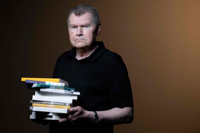 French writer Antoine Volodine poses for pictures with 11 books that will be simultaneously released in the fall of 2026, each manuscript will be published by a different publisher under the collective byline Infernus Iohannes, in Paris on June 16, 2026. (Photo by Joel Saget / AFP)