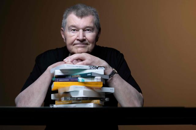 French writer Antoine Volodine poses for pictures with 11 books that will be simultaneously released in the fall of 2026, each manuscript will be published by a different publisher under the collective byline Infernus Iohannes, in Paris on June 16, 2026. (Photo by Joel Saget / AFP)