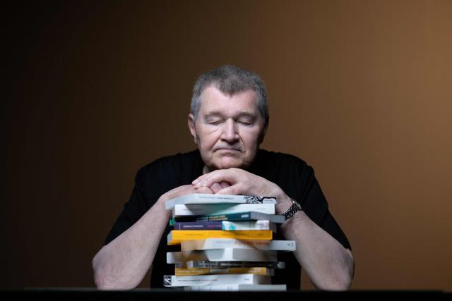 French writer Antoine Volodine poses for pictures with 11 books that will be simultaneously released in the fall of 2026, each manuscript will be published by a different publisher under the collective byline Infernus Iohannes, in Paris on June 16, 2026. (Photo by Joel Saget / AFP)