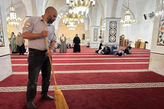 A man sweeps the floor as Palestinian women gather to celebrate the Islamic Hijri New Year at the Ibrahimi Mosque, known to Jews as the Cave of the Patriarchs, located inside the Israeli-controlled H2 sector of the occupied West Bank city of Hebron, on June 16, 2026. Israel's finance minister said on June 16, he had stripped Palestinians of authority over the site of the Cave of Patriarchs, known to Muslims as the Ibrahimi Mosque, in the occupied West Bank. The move to transfer management of the site to an Israeli committee controlled by the far-right minister, drew swift condemnation from the Palestinian Authority. (Photo by Hazem BADER / AFP)