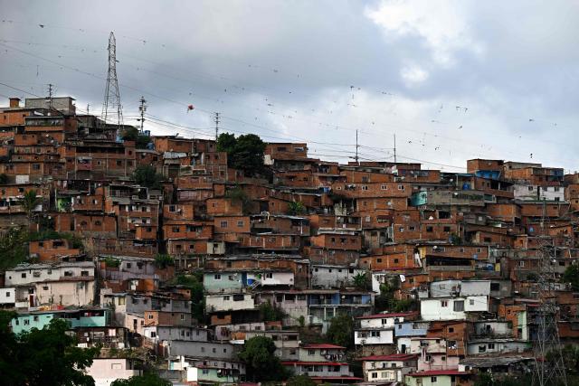 Electricity transmission towers rise above a hillside residential area in the Catia neighborhood of Caracas on June 16, 2026. Venezuela signed an agreement with US giant General Electric to begin the recovery of its beleaguered power system, acting president Delcy Rodriguez announced on June 15, 2026. (Photo by Federico PARRA / AFP)