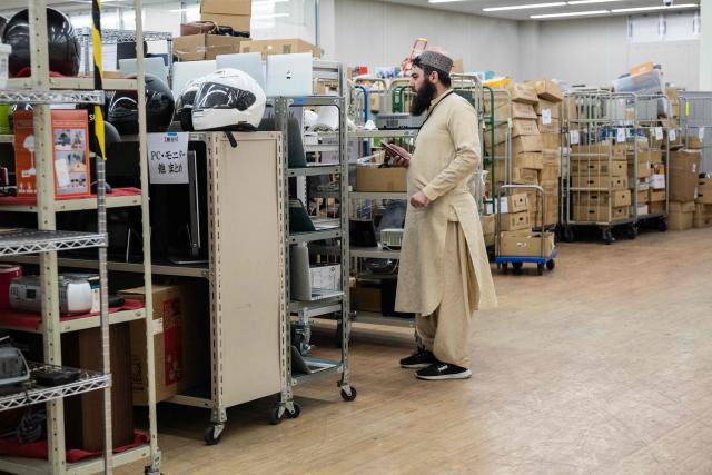 In this photo taken on May 14, 2026, an buyer searches for items among shelves of second-hand goods at the Hamaya wholesale auction site in Higashimatsuyama, Saitama Prefecture. Under a scorching sun in a Bangkok suburb, a whistle blows and shouts fill the air as dozens of shoppers rush into a warehouse bearing the sign: "Japanese Second-Hand Store". From bags and bicycles to surfboards and suitcases, the Japanese second-hand market is booming, with quality-conscious buyers in other Asian countries increasingly tapping into the circular economy trend. (Photo by Andrew CABALLERO-REYNOLDS / AFP) / To go with "JAPAN-LIFESTYLE-ENVIRONMENT-RECYCLE,FOCUS' by Montira Rungjirajittranon with Kyoko Hasegawa