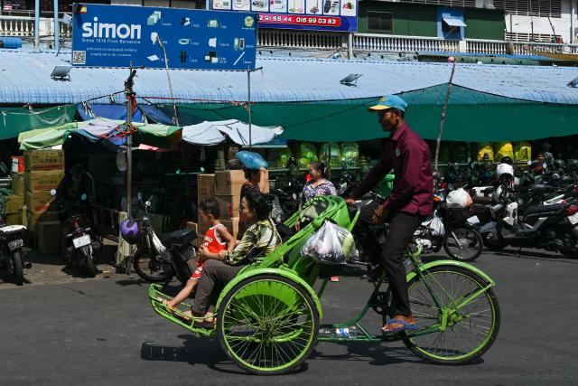 A woman and child are transported on a bicycle taxi outside a market in Phnom Penh on June 17, 2026. (Photo by TANG CHHIN Sothy / AFP)