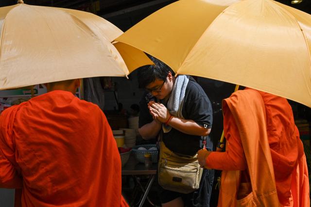 A man prays to Buddhist monks outside a market in Phnom Penh on June 17, 2026. (Photo by TANG CHHIN Sothy / AFP)