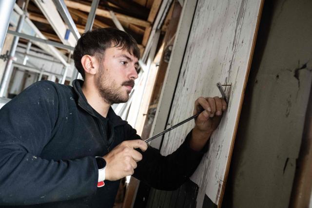 A man removes the wooden slats from the wall in the former kitchen of the Struthof concentration camp in Natzwiller, eastern France on June 4, 2026. What secrets will it reveal? The kitchen of the former Nazi concentration camp of Natzweiler-Struthof, the only one established on French soil, is undergoing a unique archaeological excavation as it is being completely restored. (Photo by SEBASTIEN BOZON / AFP)