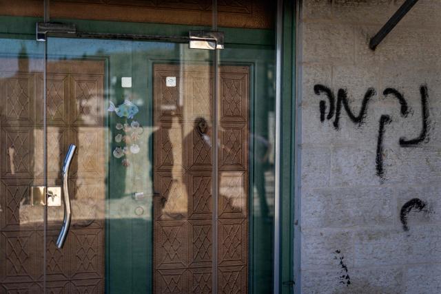 Palestinian men reflected in a window, inspect the damage to a mosque reportedly burnt by Israeli settlers over night, with Hebrew graffiti reading "nekama" or "revenge" daubed on the wall, in the Israeli occupied West Bank village of Jiljlia, just north of the West bank city of Ramallah on June 17, 2026. Expanding Israeli settlements has been a policy under successive Israeli governments but has accelerated under the current prime minister's coalition, which is backed by far-right allies. More than 500,000 Israelis now live in the West Bank. excluding east Jerusalem, in settlements that are illegal under international law, among some three million Palestinians. (Photo by ilia YEFIMOVICH / AFP) / 