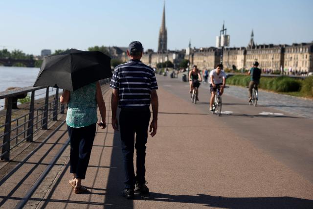 A pedestrian walks along the waterfront with an umbrella in Bordeaux, southwestern France, on June 17, 2026. A heatwave will hit France on June 17, 2026 and last for several days, right in the middle of the baccalaureate exams, with temperatures that could reach up to 40°C in some areas on Sunday, the first day of summer. (Photo by ROMAIN PERROCHEAU / AFP)