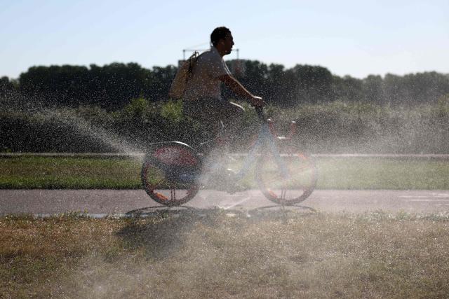 A cyclist rides his bike along the waterfront next to a sprinkler system in Bordeaux, southwestern France, on June 17, 2026. A heatwave will hit France on June 17, 2026 and last for several days, right in the middle of the baccalaureate exams, with temperatures that could reach up to 40°C in some areas on Sunday, the first day of summer. (Photo by ROMAIN PERROCHEAU / AFP)