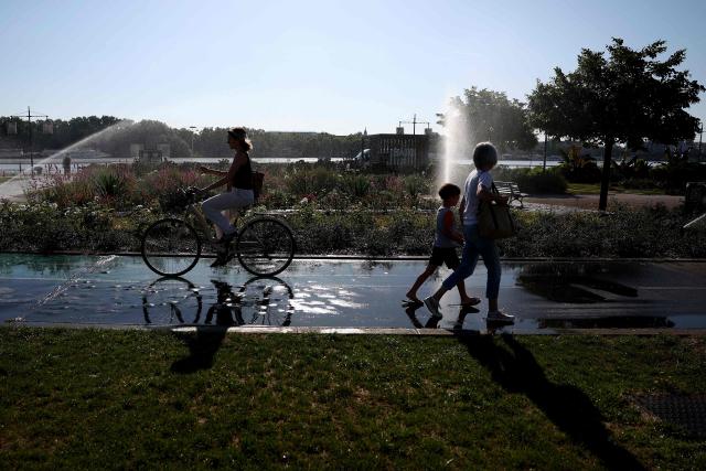 Pedestrians walk past a cyclist on the bike path, which is wet from the automatic sprinklers along the waterfront in Bordeaux, southwestern France, on June 17, 2026. A heatwave will hit France on June 17, 2026 and last for several days, right in the middle of the baccalaureate exams, with temperatures that could reach up to 40°C in some areas on Sunday, the first day of summer. (Photo by ROMAIN PERROCHEAU / AFP)