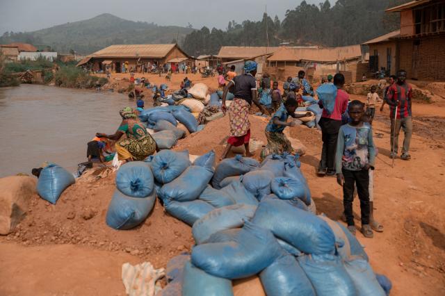 Residents and artisanal miners gather along a riverbank as bags of gold-bearing sand from nearby artisanal mines await washing and sorting before processing for gold extraction in the village of Iga Barriere, Ituri Province, on June 16, 2026. The latest Ebola outbreak in the Democratic Republic of the Congo, declared on May 15, 2026, has mainly affected the remote, conflict-weary northeastern province of Ituri. Health officials warn that population movements linked to artisanal mining, displacement and insecurity are hampering containment efforts in a region where no approved vaccine exists for this Ebola strain. (Photo by Jospin Mwisha / AFP)