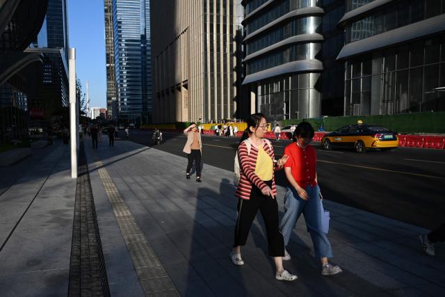 Two women walk outside an office building in Beijing on June 17, 2026. (Photo by GREG BAKER / AFP)