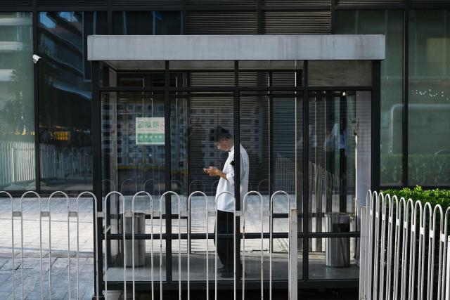 A man looks at his phone in a smoking area outside an office building in Beijing on June 17, 2026. (Photo by GREG BAKER / AFP)