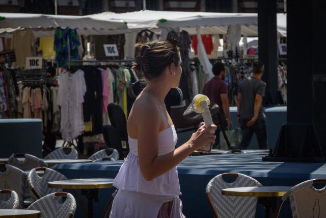 A woman holds an electric fan as she walks in the streets of Toulouse, southwestern France on June 17, 2026. A heatwave is set to hit France on June 17 and continue for several days with temperatures expected to reach up to 40°C in some areas on June 21, the first day of summer. (Photo by Ed JONES / AFP)