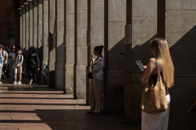 A woman holds a phone as she shelters from the sun in Toulouse, southwestern France on June 17, 2026. A heatwave is set to hit France on June 17 and continue for several days with temperatures expected to reach up to 40°C in some areas on June 21, the first day of summer. (Photo by Ed JONES / AFP)