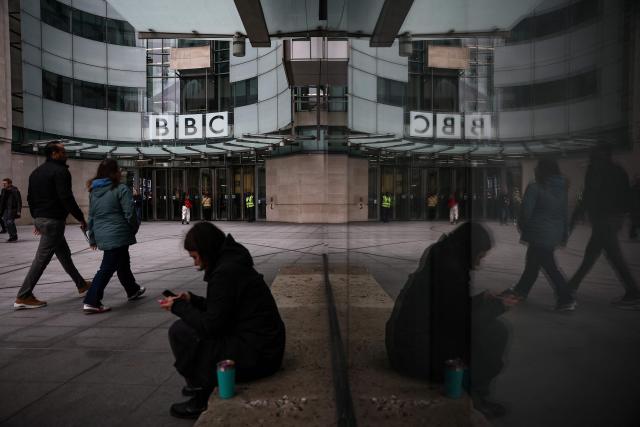 (FILES) People walk outside the entrance to the BBC offices in London on November 11, 2025. The BBC will axe some programming and may impose compulsory redundancies to deliver hundreds of millions of pounds of previously announced savings, its new Director-General Matt Brittin told staff on June 17, 2026. (Photo by HENRY NICHOLLS / AFP)