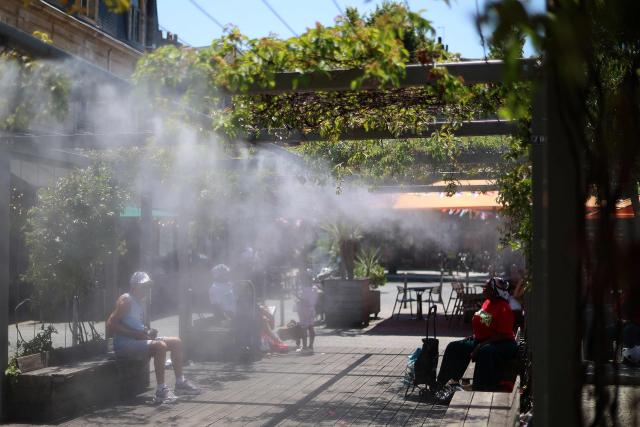 People sit in a shaded area under a water mist system to cool off in Bordeaux, south-western France, on June 17, 2026. A heatwave will hit France on June 17, 2026 and last for several days, right in the middle of the baccalaureate exams, with temperatures that could reach up to 40°C in some areas on June 21, the first day of summer. (Photo by ROMAIN PERROCHEAU / AFP)