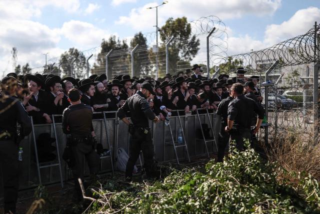 Israeli security forces stand guard as ultra-Orthodox Jews gather during a protest against military conscription outside Bet Lid military prison in Kfar Yona on June 17, 2026. Israeli lawmakers voted on June 10 to advance a bill that would allow most ultra-Orthodox Jewish men to avoid military conscription, despite fierce opposition protests. Ultra-orthodox men have largely been exempted from service throughout Israel's modern history, but the Supreme Court has repeatedly challenged that status in recent years culminating in a 2024 ruling that the government must conscript them. (Photo by Ilia YEFIMOVICH / AFP)