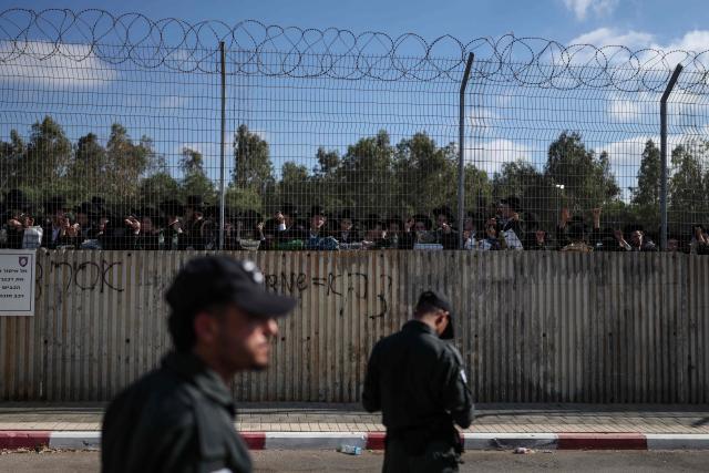 Israeli security forces stand guard as ultra-Orthodox Jews gather behind a fence during a protest against military conscription outside Bet Lid military prison in Kfar Yona on June 17, 2026. Israeli lawmakers voted on June 10 to advance a bill that would allow most ultra-Orthodox Jewish men to avoid military conscription, despite fierce opposition protests. Ultra-orthodox men have largely been exempted from service throughout Israel's modern history, but the Supreme Court has repeatedly challenged that status in recent years culminating in a 2024 ruling that the government must conscript them. (Photo by Ilia YEFIMOVICH / AFP)