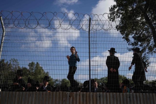 A boy peers through a fence as ultra-Orthodox Jews gather to protest against military conscription outside Bet Lid military prison in Kfar Yona on June 17, 2026. Israeli lawmakers voted on June 10 to advance a bill that would allow most ultra-Orthodox Jewish men to avoid military conscription, despite fierce opposition protests. Ultra-orthodox men have largely been exempted from service throughout Israel's modern history, but the Supreme Court has repeatedly challenged that status in recent years culminating in a 2024 ruling that the government must conscript them. (Photo by Ilia YEFIMOVICH / AFP)