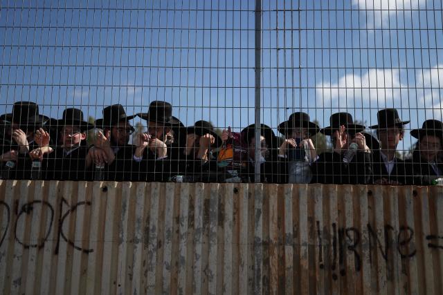 Ultra-Orthodox Jews stand behind a fence as they gather to protest against military conscription outside Bet Lid military prison in Kfar Yona on June 17, 2026. Israeli lawmakers voted on June 10 to advance a bill that would allow most ultra-Orthodox Jewish men to avoid military conscription, despite fierce opposition protests. Ultra-orthodox men have largely been exempted from service throughout Israel's modern history, but the Supreme Court has repeatedly challenged that status in recent years culminating in a 2024 ruling that the government must conscript them. (Photo by Ilia YEFIMOVICH / AFP)