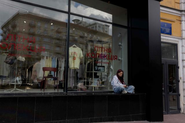 A girl sits by a store window watching her mobile phone in Kyiv on June 17, 2026, amid the Russian invasion of Ukraine. (Photo by Tetiana DZHAFAROVA / AFP)
