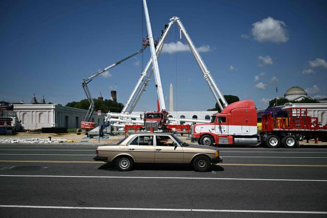 A car passes a Ferris wheel being assembled as preparations continue for the "Great American State Fair" on the National Mall in Washington, DC, June 17, 2026. The "Great American State Fair" will be held from June 25 to July 10, 2026, to celebrate the 250th anniversary of US independence. (Photo by Brendan SMIALOWSKI / AFP)