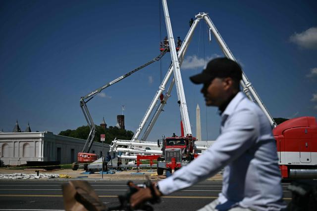 A person rides a bicycle as a Ferris wheel is being assembled as preparations continue for the "Great American State Fair" on the National Mall in Washington, DC, June 17, 2026. The "Great American State Fair" will be held from June 25 to July 10, 2026, to celebrate the 250th anniversary of US independence. (Photo by Brendan SMIALOWSKI / AFP)