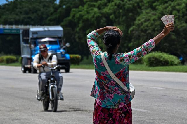A woman waits for a private lorry transporting passengers to the eastern provinces on the National Motorway on the outskirts of Havana on June 16, 2026. New restrictions on interprovincial transport in Cuba come into force on June 18, 2026, with trains running every 16 days, few weekly coaches and a state system for allocating tickets according to criteria of "urgency", amid a severe fuel shortage, under pressure from Washington. (Photo by YAMIL LAGE / AFP)