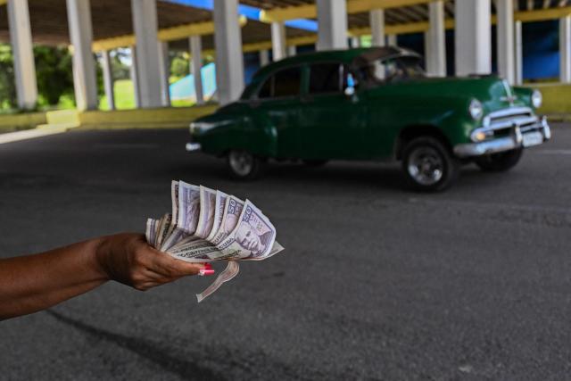 A woman holds banknotes on the National Highway on the outskirts of Havana on June 16, 2026. New restrictions on interprovincial transport in Cuba come into force on June 18, 2026, with trains running every 16 days, few weekly coaches and a state system for allocating tickets according to criteria of "urgency", amid a severe fuel shortage, under pressure from Washington. (Photo by YAMIL LAGE / AFP)