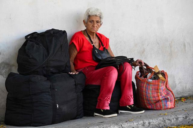 A woman sits on luggage, as she waits for transport, in Havana on June 16, 2026. New restrictions on interprovincial transport in Cuba come into force on June 18, 2026, with trains running every 16 days, few weekly coaches and a state system for allocating tickets according to criteria of "urgency", amid a severe fuel shortage, under pressure from Washington. (Photo by YAMIL LAGE / AFP)