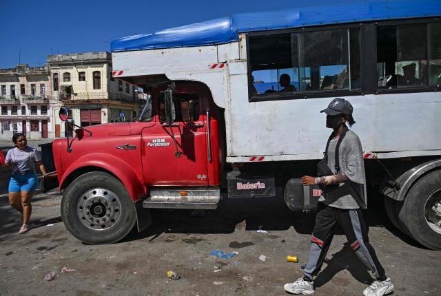 A man and a woman walk near a private lorry transporting passengers to the country's eastern provinces in Havana on June 16, 2026. New restrictions on interprovincial transport in Cuba come into force on June 18, 2026, with trains running every 16 days, few weekly coaches and a state system for allocating tickets according to criteria of "urgency", amid a severe fuel shortage, under pressure from Washington. (Photo by YAMIL LAGE / AFP)