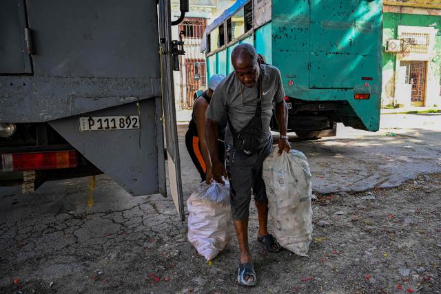 A man carries two sacks near a private lorry that transports passengers to the country’s eastern provinces, in Havana on June 16, 2026. New restrictions on interprovincial transport in Cuba come into force on June 18, 2026, with trains running every 16 days, few weekly coaches and a state system for allocating tickets according to criteria of "urgency", amid a severe fuel shortage, under pressure from Washington. (Photo by YAMIL LAGE / AFP)