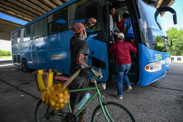 A street vendor offers mangoes to passengers on a bus on the National Highway, on the outskirts of Havana, on June 16, 2026. New restrictions on interprovincial transport in Cuba come into force on June 18, 2026, with trains running every 16 days, few weekly coaches and a state system for allocating tickets according to criteria of "urgency", amid a severe fuel shortage, under pressure from Washington. (Photo by YAMIL LAGE / AFP)