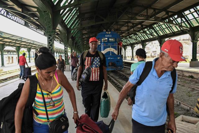Passengers, one with a T-shirt depicting the US flag, carry their luggage along a platform at the Ferrocarriles de Cuba Station in Havana on June 16, 2026. New restrictions on interprovincial transport in Cuba come into force on June 18, 2026, with trains running every 16 days, few weekly coaches and a state system for allocating tickets according to criteria of "urgency", amid a severe fuel shortage, under pressure from Washington. (Photo by YAMIL LAGE / AFP)