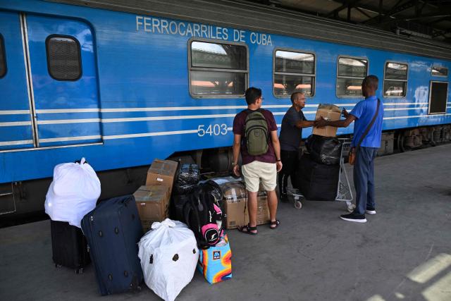 Men stand besides luggage and stacked boxes on a platform in front of a carriage of a Ferrocarriles de Cuba train, in Havana on June 16, 2026. New restrictions on interprovincial transport in Cuba come into force on June 18, 2026, with trains running every 16 days, few weekly coaches and a state system for allocating tickets according to criteria of "urgency", amid a severe fuel shortage, under pressure from Washington. (Photo by YAMIL LAGE / AFP)