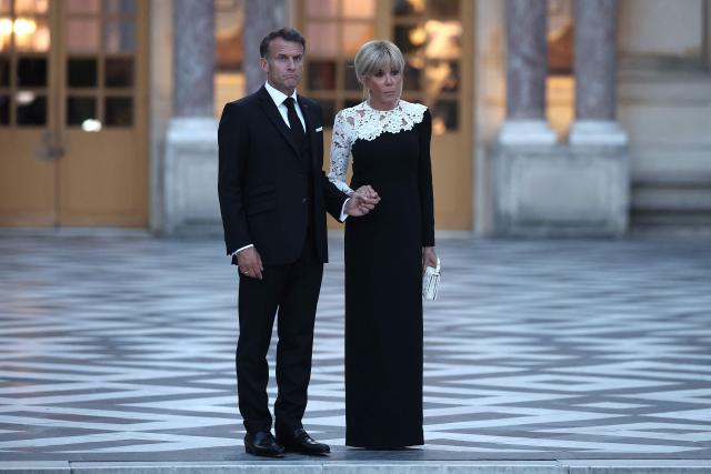 France's President Emmanuel Macron (L) reacts as he awaits the arrival of US President Donald Trump (not pictured) alongside his wife Brigitte Macron (R) ahead of a dinner to celebrate the 250th anniversary of the independence of the United States, at Chateau de Versailles in Versailles southwest of Paris on June 17, 2026. (Photo by Guillaume BAPTISTE / AFP)