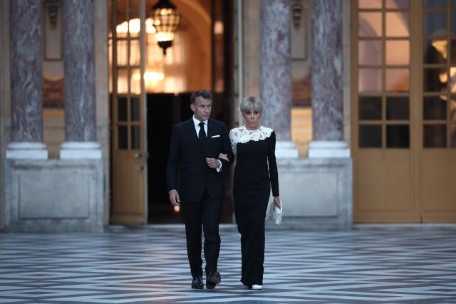 France's President Emmanuel Macron (L) and his wife Brigitte Macron (R) walk to greet the arrival of US President Donald Trump (not pictured) ahead of a dinner to celebrate the 250th anniversary of the independence of the United States, at Chateau de Versailles in Versailles southwest of Paris on June 17, 2026. (Photo by Guillaume BAPTISTE / AFP)