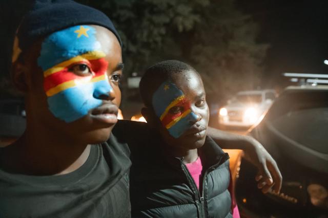 TOPSHOT - Two young boys with their faces painted in the colors of the Democratic Republic of Congo's flag look disappointed after Portugal scored during a FIFA World Cup match between DR Congo and Portugal in Bunia, Ituri Province, Democratic Republic of Congo, on June 17, 2026. The Congolese Leopards played their first match of the tournament in Houston, Texas (United States), against Portugal (1–1). The Democratic Republic of Congo (DRC) had last qualified for a World Cup in 1974. The country was then called Zaire, and the dictator Mobutu Sese Seko was in power (1965–1997). At nightfall in downtown Bunia, the capital of Ituri (northeast), a crowd gathered in the street, standing in front of a modest television screen. Above a barbecue where skewers sold individually were grilling, the owner of a small stall had hung up a screen so people could watch the match. (Photo by Jospin Mwisha / AFP)